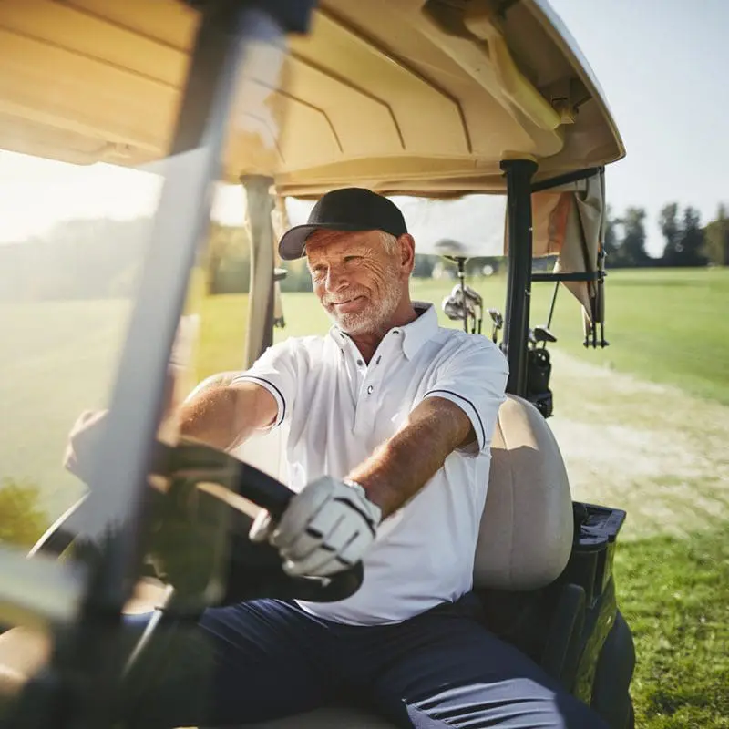 Senior man happily driving a golf cart, showcasing the active, independent lifestyle available at Windsor at Celebration senior living.