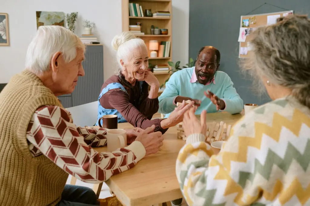 Over shoulder view of biracial companions sitting at table laughing happily while participating in a game club, looking at falling tower