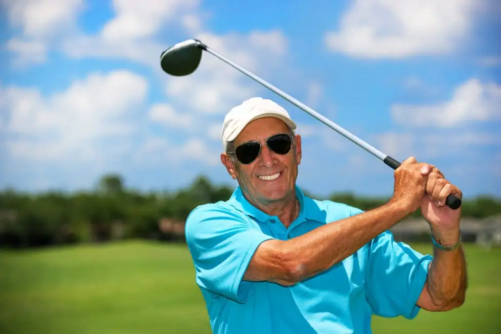 Senior man teeing off on golf course wearing sunglasses looking at the camera with a satisfied smile at Windsor at Celebration in Celebration, Florida.