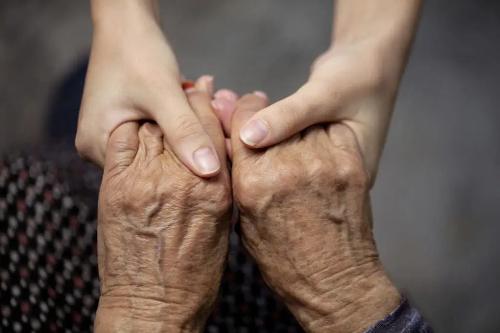 A close up of younger person holding older hands, symbolizing the importance of caring for an aging parent in retirement.
