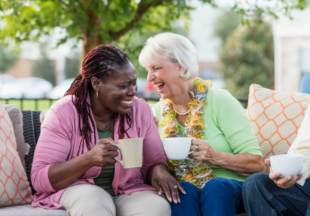 Two senior women exploring senior companionship while laughing and drinking coffee at Windsor at Celebration In Florida.